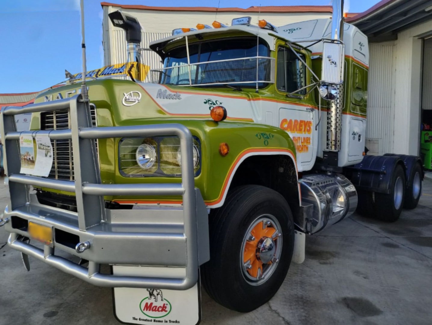 A vintage white and green Mack truck parked in front of a service bay.