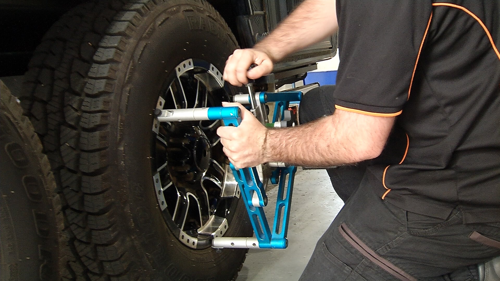 A mechanic attaches a blue wheel alignment clamp to the rim of a large off-road vehicle tyre.