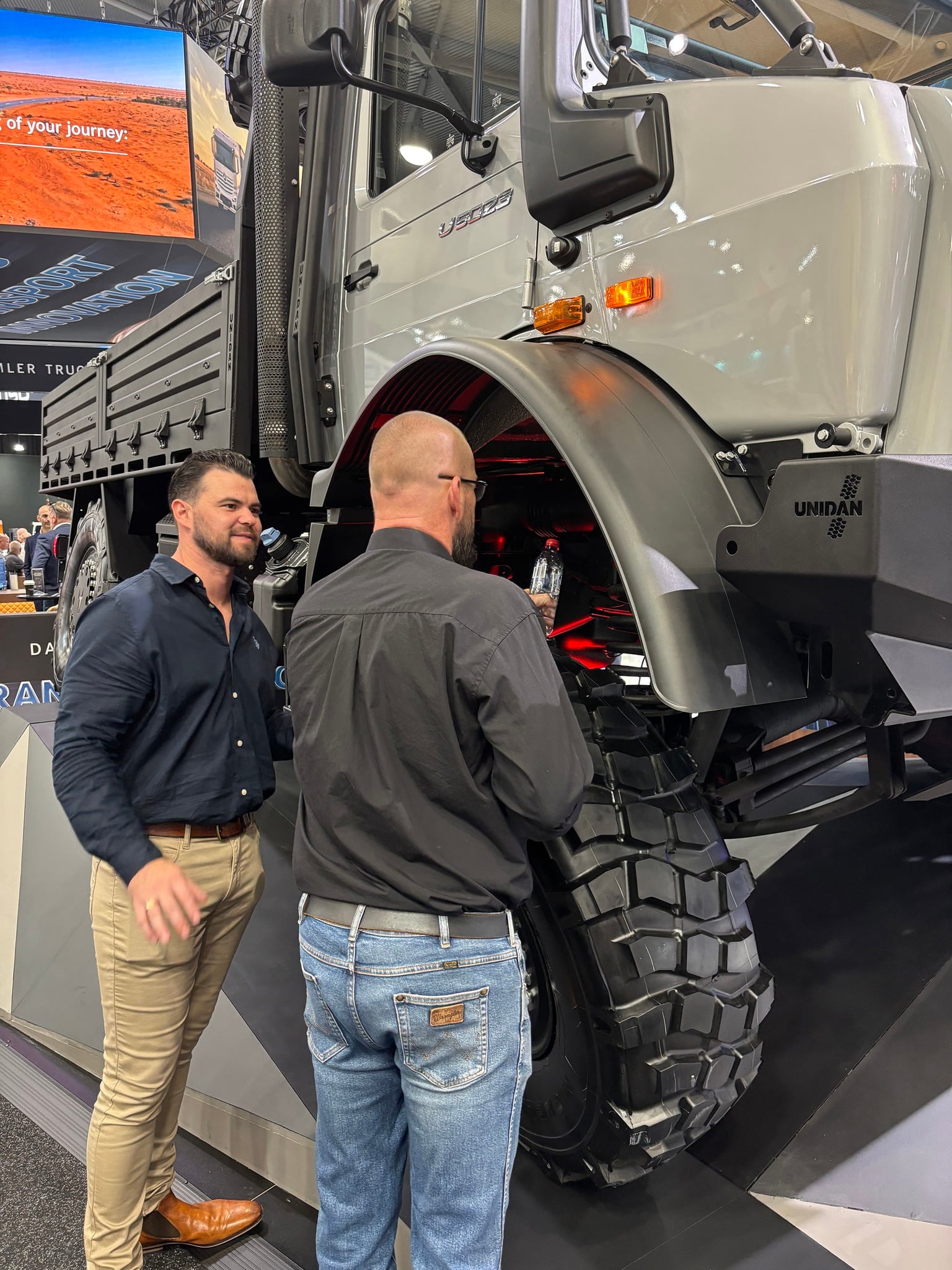 Two men standing next to a large, grey Mercedes-Benz Unimog truck