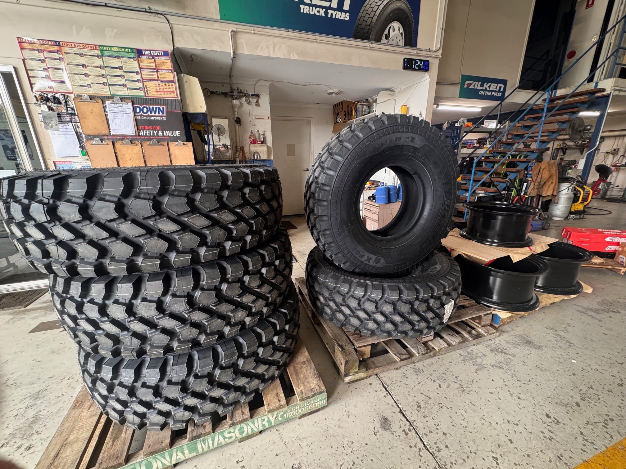 Several stacks of large, heavy-duty off-road tyres and black rims on wooden pallets.
