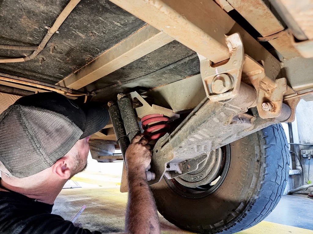 A mechanic works underneath a vehicle, inspecting the suspension system